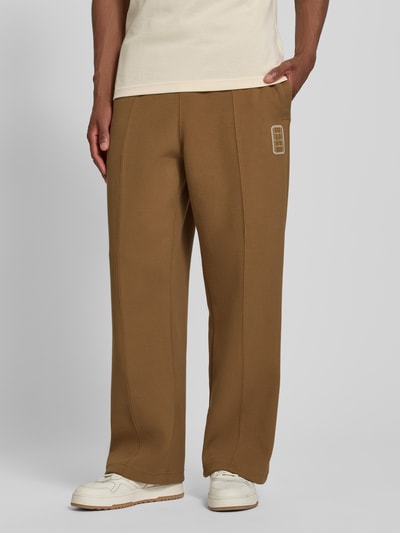 Mannenmodel draagt Loose fit Sweathose aus katoenmix model 'Tenn' van Lacoste, herensweathose, bruin, rechte pijpen, detailopname onderlichaam.