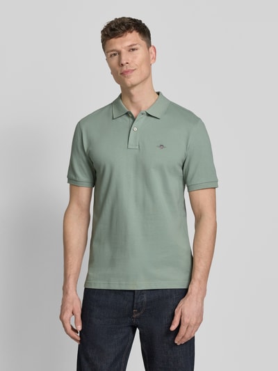 Męski model nosi Slim Fit Poloshirt mit Logo-Stitching od Gant z bawełny, krój slim fit, kołnierzyk polo, krótki rękaw, długość tyłu 70 cm, zielony, gładki materiał, Ganzkörperansicht von vorne