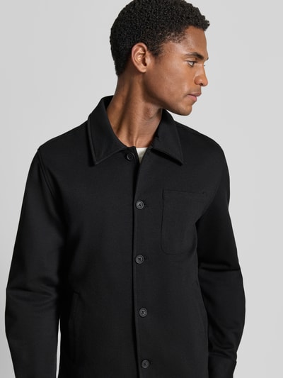 Männermodel trägt Slim Fit Hemdjacke mit Viskose-Anteil von Lindbergh in Schwarz, glatte Knopfleiste, Aufgesetzte Brusttasche, Nahaufnahme Oberkörper.