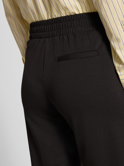 Vrouwenmodel draagt Stoffhose mit Eingrifftaschen van ICHI, uni zwart, elastische tailleband, materiaal-mix met viscose, detailopname taille en heup.
