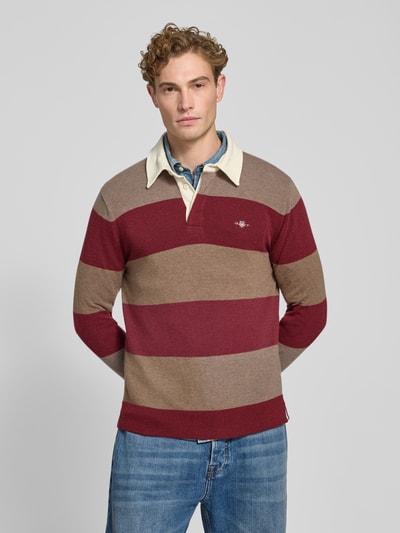 Männermodel trägt Regular Fit Pullover aus reiner Baumwolle von GANT in Beige und Rot mit breiten Streifen, Ganzkörperansicht von vorne.