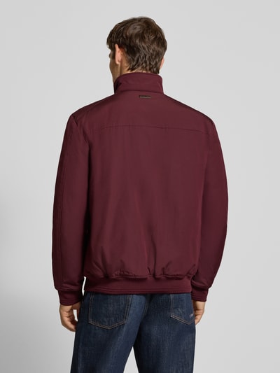Männermodel trägt Regular Fit Jacke mit Stehkragen von Christian Berg Men in Dunkelrot, glatte Textur, Ganzkörperansicht Rückansicht. Herren Jacke mit Eingrifftaschen, Reißverschluss, elastischen Abschlüssen, Rückenlänge 69 cm, Schulterbreite 49 cm, Brustweite 55 cm, Ärmellänge 67 cm.