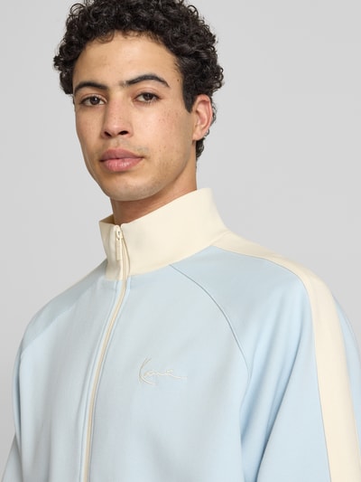Männermodel trägt Regular Fit Sweatjacke mit Logo-Stitching von KARL KANI in Hellblau und Creme, Elastischer-Material-Mix, Nahaufnahme Oberkörper.