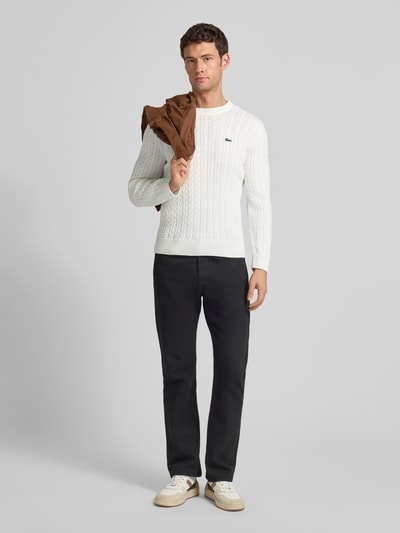 Männermodel draagt Regular Fit gebreide pullover uit katoenmix van Lacoste, effen look, kabelpatroon, logopatch, lange mouw, ronde hals, geribde boorden, labelstitching, contrastnaad; herenmode, Ganzkörperansicht van voren.