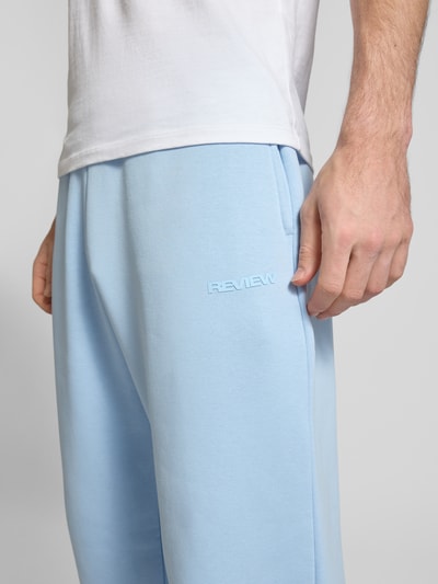 Mężczyzna nosi spodnie dresowe Sweatpants aus Baumwoll-Mix od REVIEW, jasnoniebieskie, mieszanka bawełny, boczne kieszenie, detal z logo, zbliżenie na biodra
