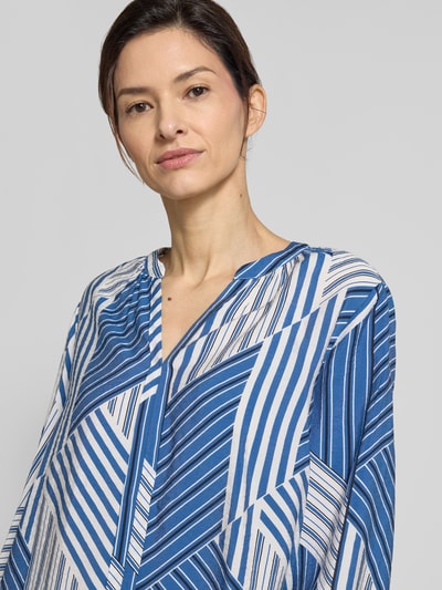 Modelka kobieca ma na sobie niebiesko-białą Relaxed Fit Langarmbluse aus Viskose-Mix von s.Oliver RED LABEL, wzory geometryczne, dekolt V, detal na środku, zdjęcie zbliżeniowe górnej części ciała.