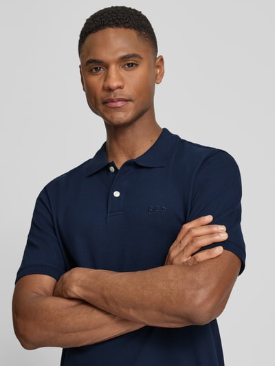 Männermodel trägt Slim Fit Poloshirt mit Label-Stitching von GAP, Baumwoll-Elasthan-Mix, Knopfleiste, dunkelblau, Nahaufnahme Oberkörper.