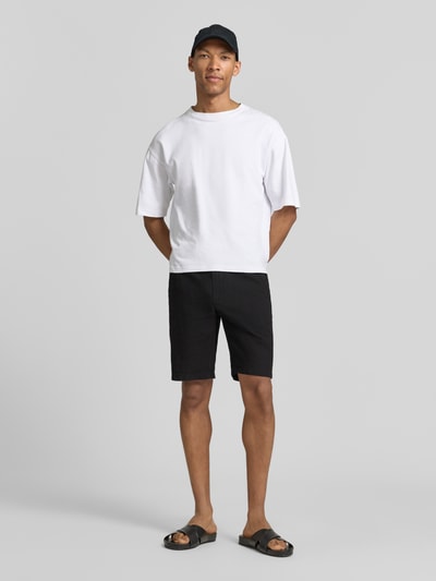 Männermodel trägt Bermudas aus Leinen-Mix mit französischen Eingrifftaschen von Lindbergh, mieszanka lnu i bawełny, krój straight fit, elastyczny pas z trokiem, zapięcie na guzik i zamek błyskawiczny, wpuszczane kieszenie, kieszenie z tyłu, szerokość w rozmiarze M: 43 cm, długość wewnętrzna nogawki w rozmiarze M: 24 cm, kolor czarny, faktura gładka, całopostaciowy widok z przodu.