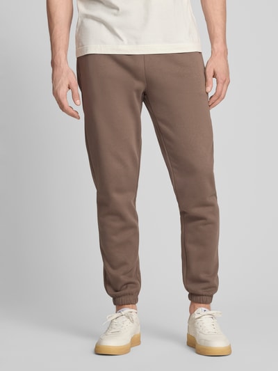 Mężczyznamodel nosi Sweatpants mit Eingrifftaschen von GAP z mieszanki bawełny, krój regular fit, brązowe, wpuszczane kieszenie, logo, długość wewnętrzna nogawki 72 cm w rozmiarze M, całkowity widok z przodu
