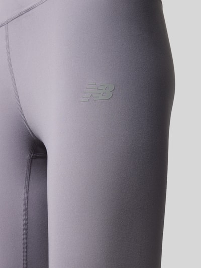 Frauenmodel trägt Slim Fit Leggings mit Logo-Print Modell 'Harmony' von New Balance, grauer Jersey-Stoff, Nahaufnahme Oberschenkel.