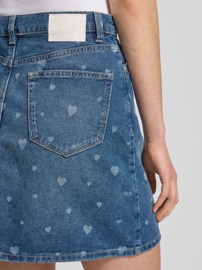 Frauenmodel trägt Mini-Jeansrock aus reiner Baumwolle von Tom Tailor Denim mit Optik:Allover-Muster Herzmuster, 5-Pocket-Design, Label-Patch, Nieten, gerade, Denim, Nahaufnahme Rückansicht.