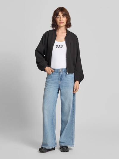 Frauenmodel trägt Tanktop mit Logo-Print und Rundhalsausschnitt von GAP in Weiß, körpernaher Schnitt, Feinripp, Nahaufnahme Oberkörper.
