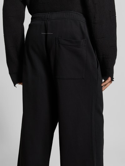 Männermodel trägt Wide Fit Stoffhose mit Gesäßtasche von MM6 Maison Margiela, Reine Baumwolle, Elastischer Bund, Detailaufnahme Rückansicht.