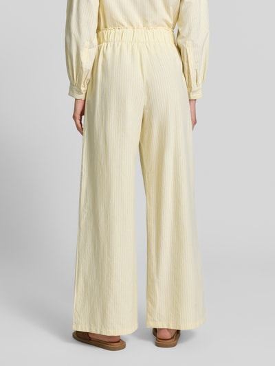 Frauenmodel trägt Wide Leg Stoffhose aus Baumwoll-Mix Modell 'STELLA' von VILLA SOPHIE mit Allover-Muster, elastischem Bund und seitlichen Eingrifftaschen, cremig-gelbe Streifenoptik, Ganzkörperansicht Rückansicht.