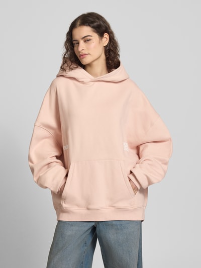 Frauenmodel trägt Oversized Hoodie mit Känguru-Tasche von Karo Kauer in zartem Rosa, reine Baumwolle, Label-Print, Ganzkörperansicht von vorne