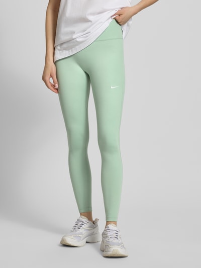 Frauenmodel trägt Leggings mit Logo-Print Modell 'One' von NIKE TRAINING, grüner Material-Mix mit Stretch-Anteil, Slim-Fit, elastischer Bund, Nahaufnahme Unterkörper.