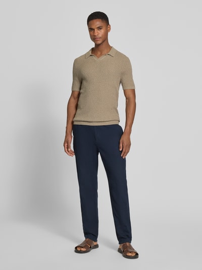 Männermodel trägt Slim Fit Strick-Poloshirt mit Strukturmuster von bugatti in Beige, Baumwoll-Mix, kombiniert mit dunkler Hose, Ganzkörperansicht von vorne.