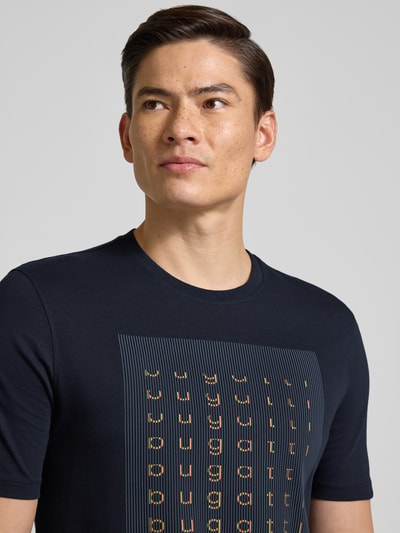Männermodel trägt Regular Fit T-Shirt mit Logo-Print von bugatti aus Reine Baumwolle, Rundhalsausschnitt, Herren T-Shirt, Nahaufnahme Oberkörper. Rückenlänge bei Größe M: 70 cm.