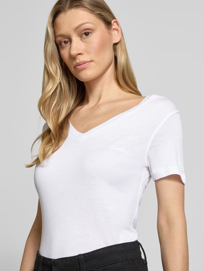 Kobiece modelka nosi Slim Fit T-Shirt aus reinem Lyocell od Guess, damski t-shirt, krój slim fit, dekolt w serek, wyhaftowane logo, długość tyłu 58 cm w rozmiarze S, biała gładka tekstura, delikatny połysk, prosty krój. Nahaufnahme Oberkörper.