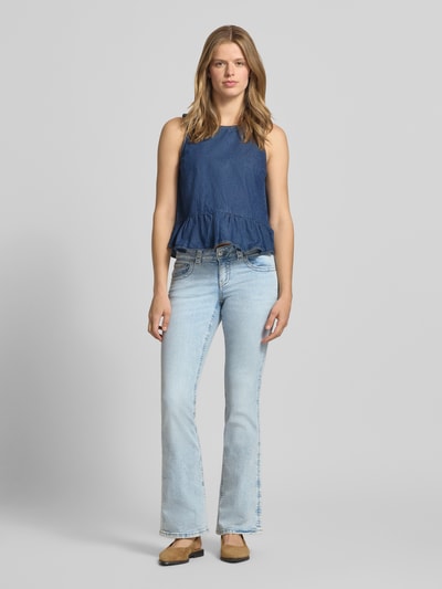 Frauenmodel trägt Low Bootcut Jeans mit Eingrifftaschen Modell 'Y2k' von Gina Tricot in hellem Blau, Baumwoll-Elasthan-Mix, Ganzkörperansicht von vorne. Bundweite bei Größe 36: 37 cm, Innenbeinlänge bei Größe 36: 83 cm.