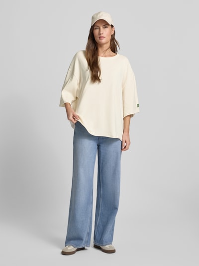 Frauenmodel trägt Oversized T-Shirt mit Label-Print von American Vintage in Creme, kombiniert mit weiter Jeans, lockere Textur, Ganzkörperansicht von vorne. Reine Baumwolle, gerippter Rundhalsausschnitt, Rückenlänge bei XS/S: 65 cm.