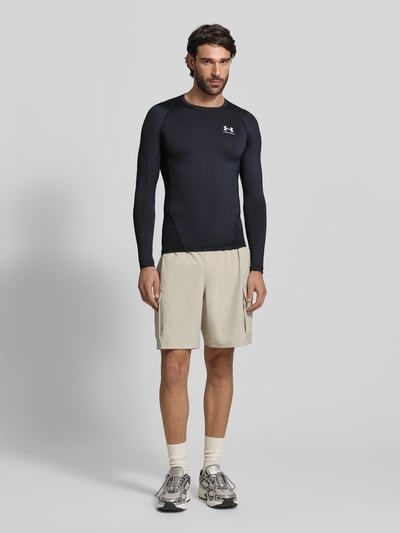 Männermodel trägt Slim Fit Longsleeve mit Logo-Print von Under Armour in Schwarz, elastischer Material-Mix, Rundhalsausschnitt, Ganzkörperansicht von vorne.