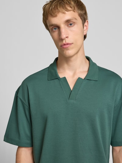 Męski model nosi Boxy Fit Poloshirt aus Baumwoll-Mix Modell 'CASPIAN AIRLEX' von Only & Sons, gładka zieleń, krótki rękaw, polokrągły kołnierz, jersey, naszywka z logo, Nahaufnahme Oberkörper.