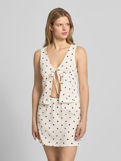 Kobiece modelka nosi Blusentop mit V-Ausschnitt und Schnürung Modell 'SOPHIE' von Noisy May, mieszanka materiałów z dodatkiem streczu, krój straight fit, dekolt w serek, wiązanie, długość tyłu w rozmiarze S: 49 cm, białe tło, czarne kropki, widok całej sylwetki z przodu.