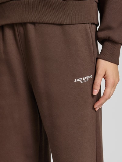 Frauenmodel trägt Wide Fit Sweatpants aus Baumwoll-Mix Modell 'Studio' von JJXX in Braun mit Logo-Detail, Nahaufnahme Oberschenkel. Damen Sweatpants von JJXX, Baumwoll-Mix, Wide Fit, Modell 'Studio', Logo-Detail, elastischer Bund, Innenbeinlänge bei Größe S: 38 cm.