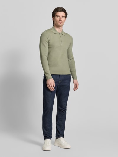 Männermodel trägt Slim Fit Pullover mit Polokragen Modell 'GUNA' von Samsøe Samsøe, grün, Reißverschluss, Ganzkörperansicht von vorne.