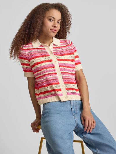 Modelka kobieca nosi Regular Fit Poloshirt aus Strick Modell 'LULA' od Only, wzór w paski, ażurowa dzianina, różowo-czerwone odcienie, krótki rękaw, kołnierzyk polo, żebrowane wykończenia, krój regular fit, widok na górną część sylwetki z przodu.