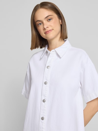 Frauenmodel trägt Loose Fit Jeanskleid aus Baumwoll-Mix Modell 'SKY' von Pieces in Weiß, strukturierte Knopfleiste, Nahaufnahme Oberkörper.