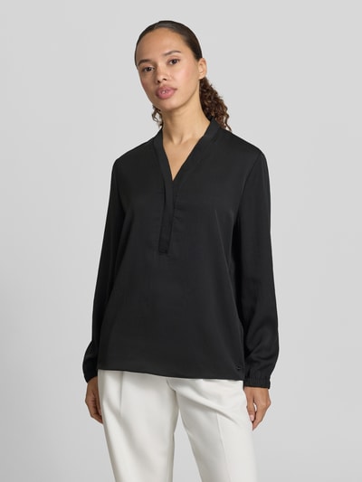 Frauenmodel trägt Bluse mit V-Ausschnitt und Label-Detail von Marc Cain in Schwarz, elastische Ärmelabschlüsse, Loose Fit, Ganzkörperansicht von vorne