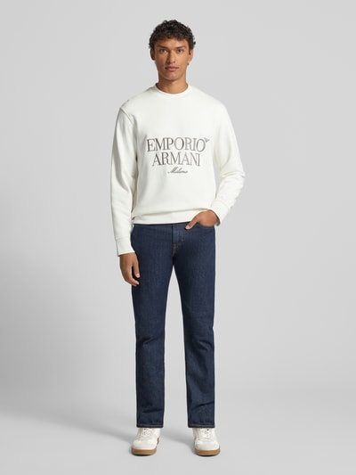 Männermodel trägt Sweatshirt mit Label-Stitching von Emporio Armani, weiße Baumwolle, lockerer Schnitt, gerippte Abschlüsse, Rundhalsausschnitt, Ganzkörperansicht von vorne.