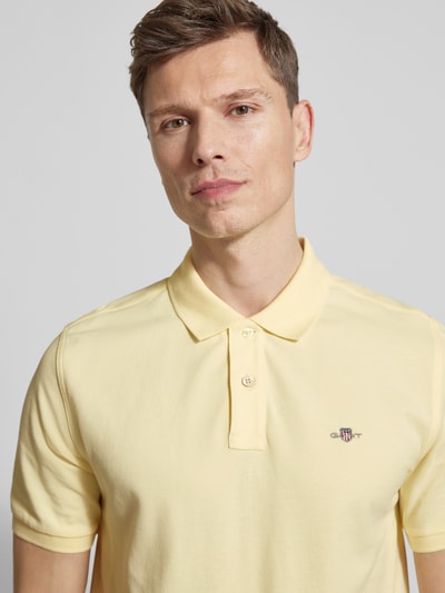 Männermodel trägt Slim Fit Poloshirt mit Logo-Stitching von Gant in Hellgelb, reine Baumwolle, Polo-Kragen, Nahaufnahme Oberkörper.