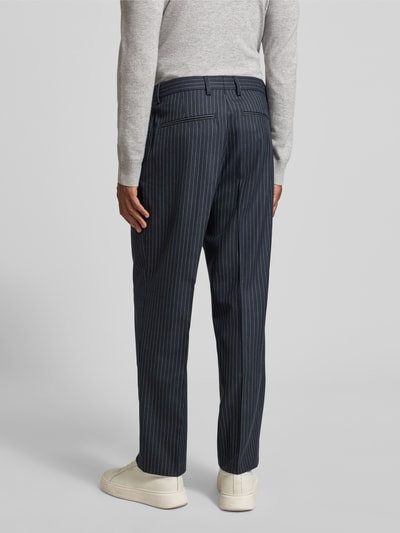 Męski model nosi szerokie spodnie z mieszanki wełny 220-LOOSE OTTO LANO PL od SELECTED HOMME, wzór w cienkie prążki, denim, efekt: wzór na całej powierzchni, krój loose fit, szlufki na pasek, wpuszczane kieszenie; widok całej sylwetki z tyłu.
