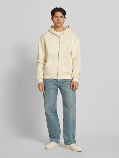 Mężczyznamodel nosi Sweatjacke mit Label-Print od REVIEW, mieszanka bawełny, prosty krój, kaptur, zamek błyskawiczny, wpuszczane kieszenie, prążkowane wykończenia, długość tyłu w rozmiarze M: 60 cm, długość rękawów w rozmiarze M: 63 cm, jasne kolory, gładka tekstura, widok całej sylwetki z przodu.