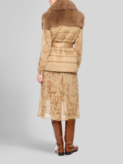 Frauenmodel trägt Weste aus Kunstfell mit Bindegürtel von Marc Cain in Beige mit Schalkragen, über gemustertem Kleid, Ganzkörperansicht Rückansicht. Rückenlänge 68 cm, Schulterbreite 46 cm, Brustweite 55 cm.