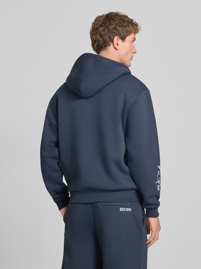 Männermodel trägt Relaxed Fit Sweatjacke mit Kapuze von REVIEW in Dunkelblau, florale Stickerei, Rückenansicht, Baumwoll-Mix.