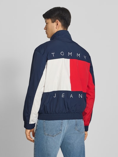 Männermodel trägt Regular Fit Blouson mit Logo-Stitching van Tommy Hilfiger in effen kleuren, satijn materiaalverwerking, rompzoom en mouwboord elastisch, zijsteekzakken met drukknoopsluiting, opstaande kraag, logo-applicatie, lange mouw, achterkant, Ganzkörperansicht Rückansicht.