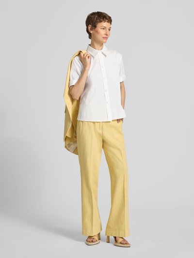 Frauenmodel trägt Bluse mit verlängertem Rücken und Kentkragen von Windsor aus weißem Baumwoll-Mix mit Stretch, Straight Fit, Halbarm, Knopfleiste, kombiniert mit gelber Hose, Ganzkörperansicht von vorne.