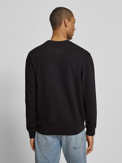 Männermodel trägt Regular Fit Sweatshirt mit Rundhalsausschnitt von Scotch & Soda aus katoenmix, labeldetail, ruglengte 68 cm, mouwlengte 65 cm, ganzlichaamsaanzicht achteraan.