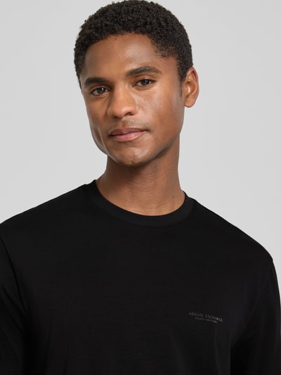 Männermodel trägt Extra Slim Fit T-Shirt mit Rundhalsausschnitt von Armani Exchange, schwarzer Stoff, dezentes Logo-Print, Nahaufnahme Oberkörper, Rückenlänge bei Größe M 70 cm.