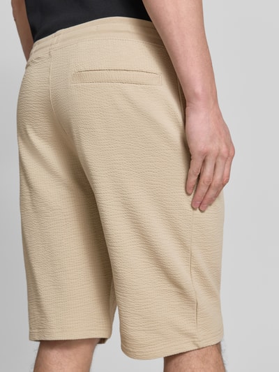 Männermodel trägt Relaxed Fit Bermudas aus Baumwoll-Mix Modell 'DETROIT' von s.Oliver RED LABEL, beige Waffelstruktur, Ganzkörperansicht Rückansicht.