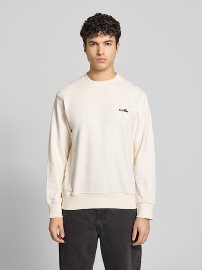 Męski model nosi Sweatshirt mit Rundhalsausschnitt und Label-Stitching od Ellesse, beżowy bawełniany miks, krój regular fit, dekolt okrągły, logo na piersi, długość tyłu w rozmiarze M: 66 cm, długość rękawa w rozmiarze M: 64 cm, całkowity widok z przodu.