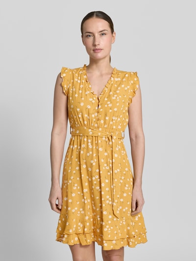 Frauenmodel trägt Minikleid aus Viskose mit Bindegürtel und Kappärmeln von Apricot, gelb mit weißen Blumen, Taillierter Schnitt, V-Ausschnitt mit Rüschen, kurze Knopfleiste, Stufenrock, Rückenlänge 89 cm, Brustweite 38 cm, Ganzkörperansicht von vorne.