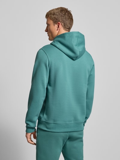 Männermodel trägt Hoodie mit Kapuze von CHAMPION in Türkis, Baumwoll-Mix, Lockerer-Schnitt, Känguru-Tasche, Ganzkörperansicht Rückansicht.