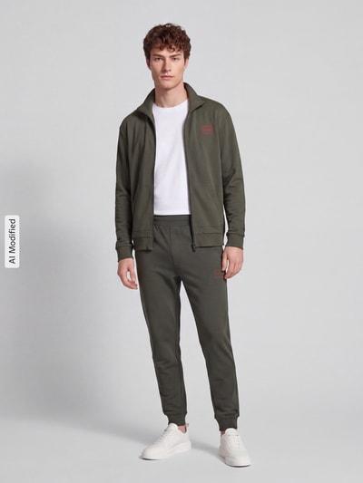 Męski model nosi Regular Fit Sweathose aus Baumwoll-Mix model 'Laze Pants CW' od HUGO, kolor oliwkowy, tekstura gładka, Ganzkörperansicht von vorne, spodnie HUGO Herren, KI-modifiziertes Bild.