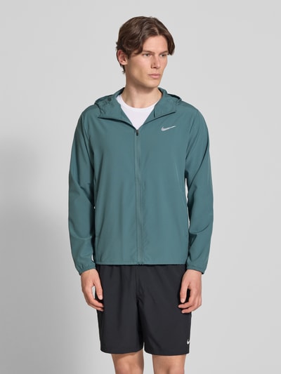 Männermodel trägt Trainingsjacke mit Logo-Print und Stehkragen von NIKE TRAINING in Grün mit Reißverschluss, gerader Schnitt, seitliche Eingrifftaschen, elastische Ärmelabschlüsse, Rückenlänge 69 cm bei Größe M, Ärmellänge 65 cm bei Größe M, Ganzkörperansicht von vorne.