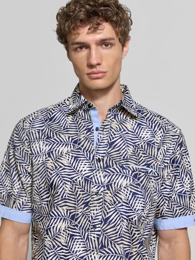 Mężczyznamodel nosi Modern Fit Freizeithemd mit Kentkragen od Christian Berg Men z bawełny, wzór liści, listwa guzikowa, brustasza, długość tyłu 79 cm, szerokość w rozmiarze M 49 cm, długość rękawów 27 cm, zbliżenie na górną część ciała